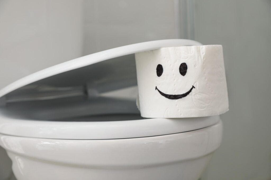 Roll of paper with drawn funny face on toilet seat in bathroom