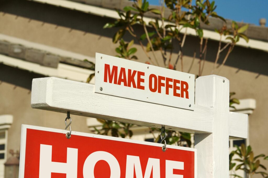 Make an Offer Real Estate Sign in Front of Beautiful New Home.