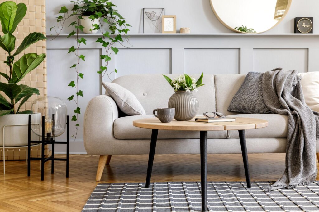 Stage your home for a quick sale. Scandinavian living room interior with design grey sofa, wooden coffee table, tropical plants, shelf, mirror, furniture, plaid pillow, teapot, book and elegant personal accessories in home decor.